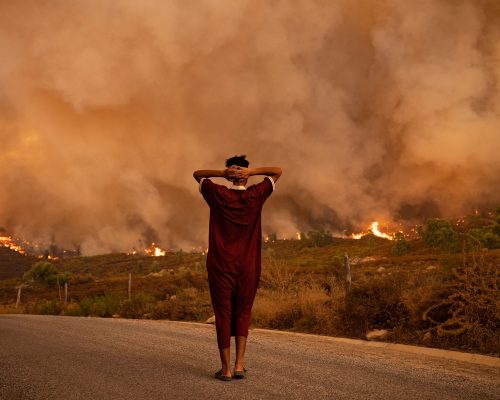 TOPSHOT - A woman looks at wildfires tearing through a forest in the region of Chefchaouen in northern Morocco on August 15, 2021. - Firefighters were battling overnight to put out two forest blazes, a forestries official said as the North African kingdom swelters in a heatwave that saw temperatures of up to 49 degrees Celsius (120 Fahrenheit) on the weekend, according to weather authorities. Morocco joins several other Mediterranean countries that have seen forest fires in recent weeks, including neighbouring Algeria where at least 90 people were killed in wildfires last week. (Photo by FADEL SENNA / AFP) (Photo by FADEL SENNA/AFP via Getty Images)